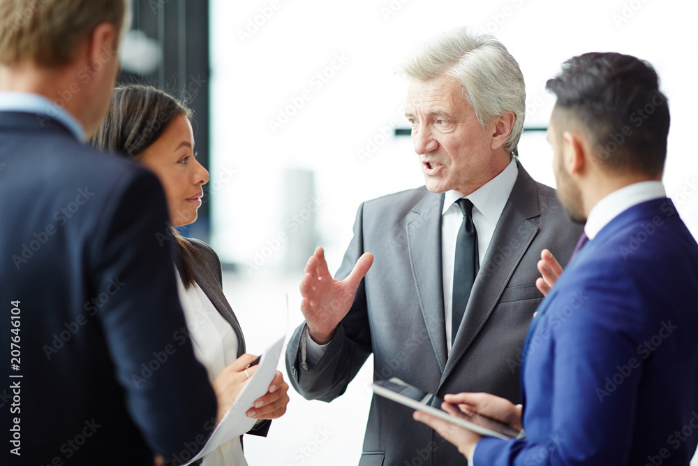 Fototapeta premium Confident grey-haired businessman explaining working moments to his subordinates before business conference