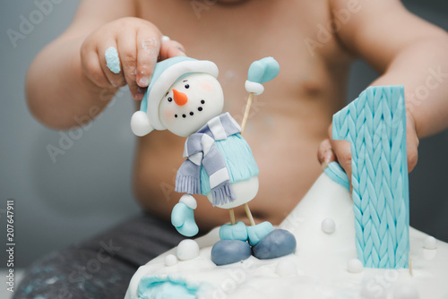 Cute little boy eating his first birthday cake. Baby cake smash. Birthday cake for 1 year old boy. Winter cake with a snowman.