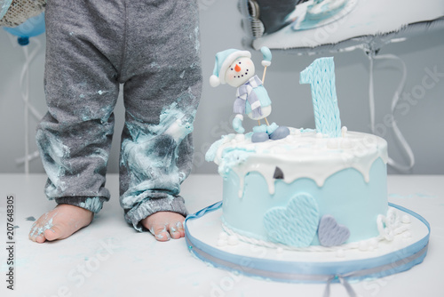 Kid's feet near the cake. Cute little boy eating his first birthday cake. Baby cake smash. Birthday 1 year old boy. Winter cake with a snowman. photo