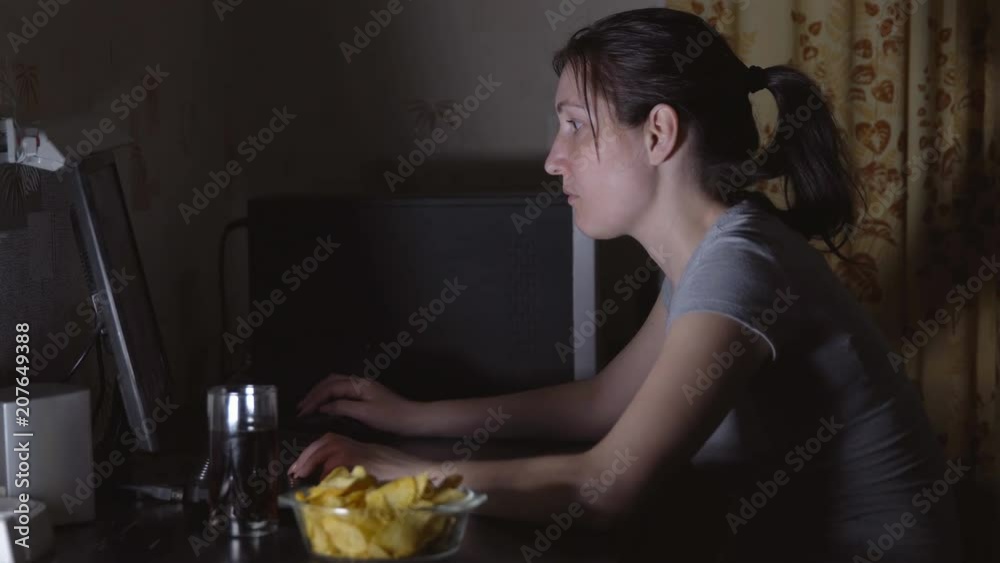 Young woman sitting at the computer and eating chips. Young woman sitting at the computer and eating chips.