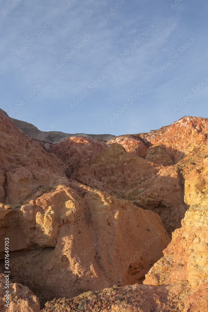 Small ravine in multicolored red, orange and yellow striped hills under a bright blue sky in Eastern Kazakhstan