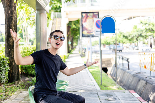 Handsome man is roistering bus that come to lately. Cool guy get mad because he is waiting for long time and weather is so hot in summer season. He is unsatisfied the system of public transportation photo