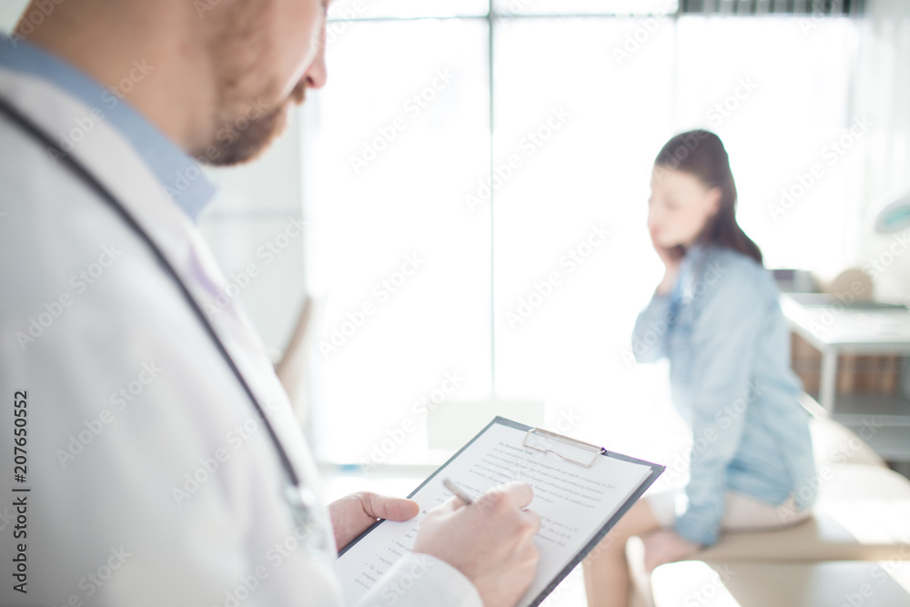Modern clinician writing down prescriptions for one of his patients Modern clinician writing down prescriptions for one of his patients
