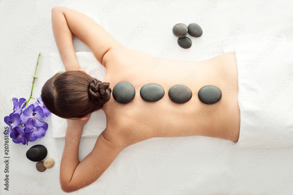 Stone treatment. Top view of beautiful young woman lying on front with spa stones on her back.  Beauty treatment concept. - obrazy, fototapety, plakaty 