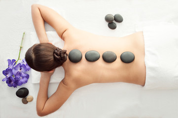 Foto auf Acrylglas Massagesalon Steinbehandlung. Blick von oben auf die schöne junge Frau, die auf der Vorderseite mit Spa-Steinen auf dem Rücken liegt. Schönheitsbehandlungskonzept.  © Mariana