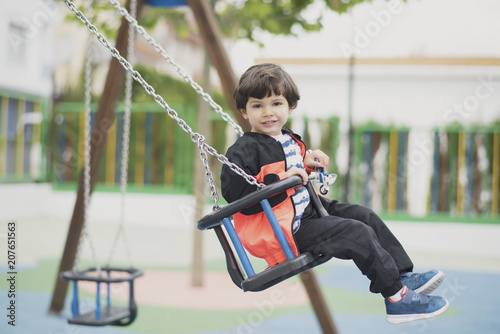 Preschooler little boy having fun swinging at the park photo