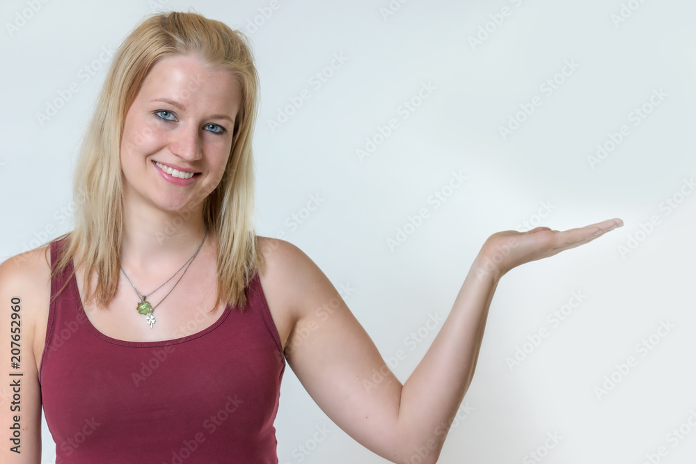 Studio shot of the attractive young blond woman posing with open hand in sportswear. Woman is smiling at the camera. Studio shot of the attractive young blond woman posing with open hand in sportswear. Woman is smiling at the camera.