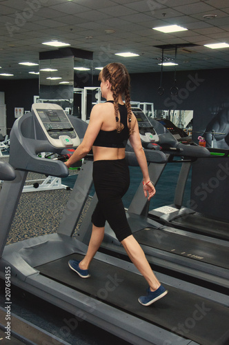 Fitness woman is engaged on a treadmill in the gym. Rear view and side view.