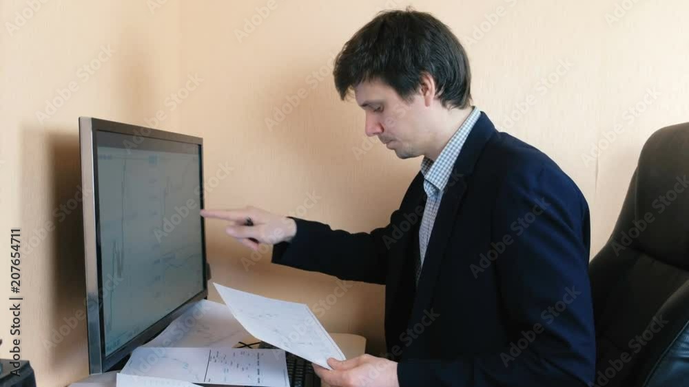 Man works at a computer. Compares graphics on the screen and on paper. Man works at a computer. Compares graphics on the screen and on paper.