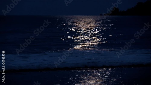 Full moon reflection on a Caribbean Beach.  White wake on the waves of the sea in the tropics. Waves breaking on the shore in the light of the moon.
