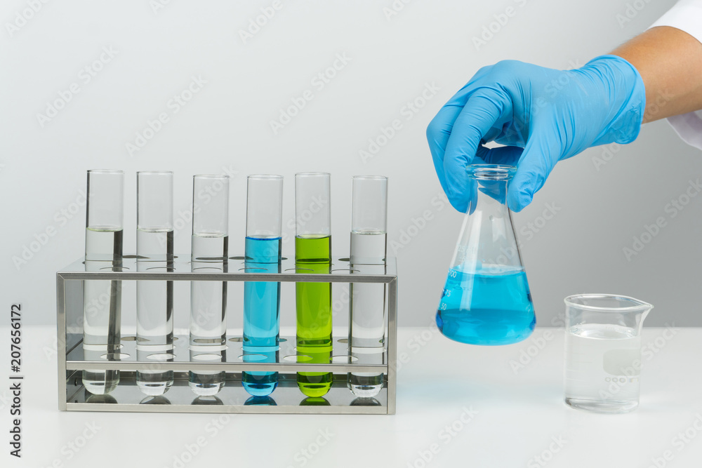 laboratory scene, the scientist holding the blue liquid flask, test tubes in the rack and beaker on the table laboratory scene, the scientist holding the blue liquid flask, test tubes in the rack and beaker on the table