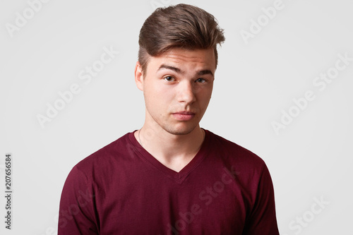Portrait of fashionable male teenager has trendy haircut, healthy skin, wears casual t shirt, looks confidently at camera, going to have date with girlfriend, isolated over white background. © sementsova321
