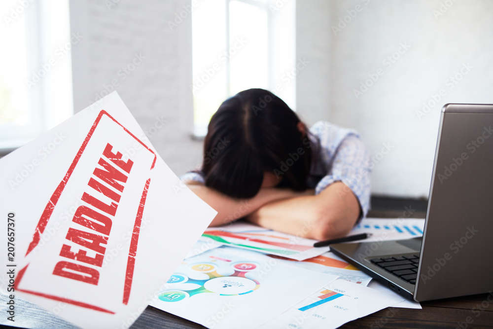 Tired disturbed female worker lying her head on the table.Stressed woman in office thinking about deadline.Overwork,burnout,negative thoughts, deadline concept.