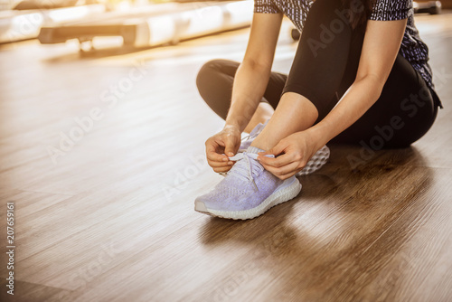 Woman tying running shoes on black floor background in gym with sunlight. copy space.