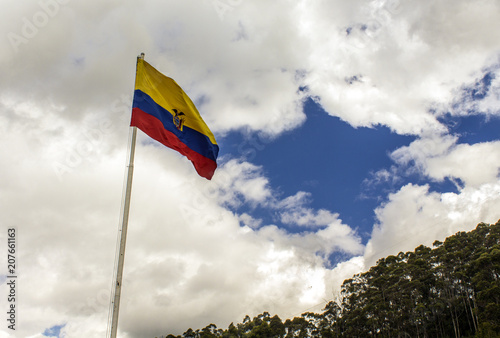 Flag of the Republic of Ecuador, on a sunny day with the city of Quito in the background.