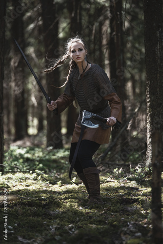 Schilderij op canvas Viking woman with sword and hammer wearing traditional warrior clothes in a deep mysterious forest