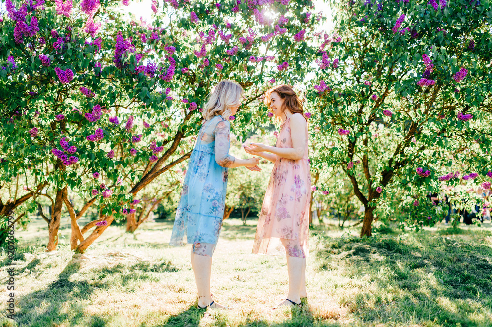Fototapeta premium Happy family outdoor. Twin sisters have fun at nature. Beautiful twins in dresses dancing. Lovely cheerful young girls enjoying childhood outdoor in summer. Two cute women laughing and smiling.