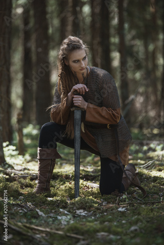 Schilderij op canvas Viking woman with sword wearing traditional warrior clothes in a deep mysterious forest