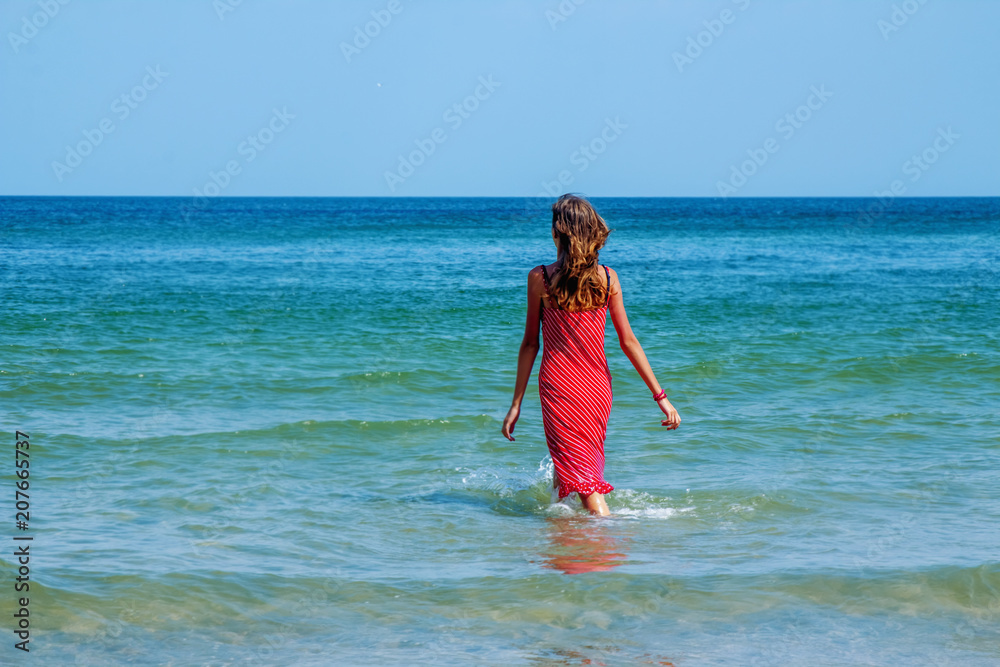 Sunny summer portrait of happy beautiful young brunette girl having fun on the beach of blue sea. (travel, happiness, summer rest, freedom concept).