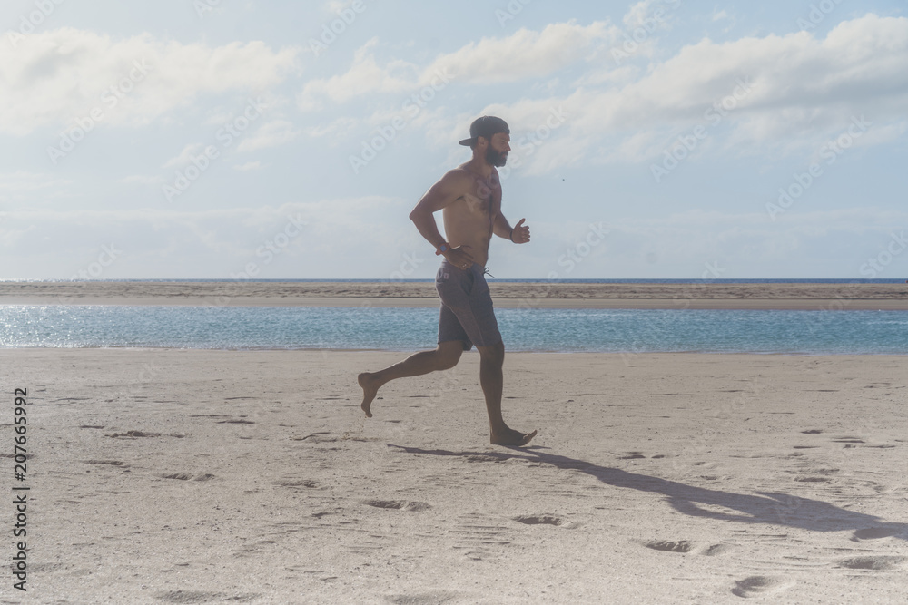 Young runner running in morning along the beach. Young bearded man jogging on the sea shore at sunrise Young runner running in morning along the beach. Young bearded man jogging on the sea shore at sunrise
