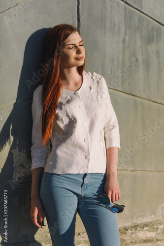 Young beautiful girl is basking in the sun. Portrait of a model near the wall