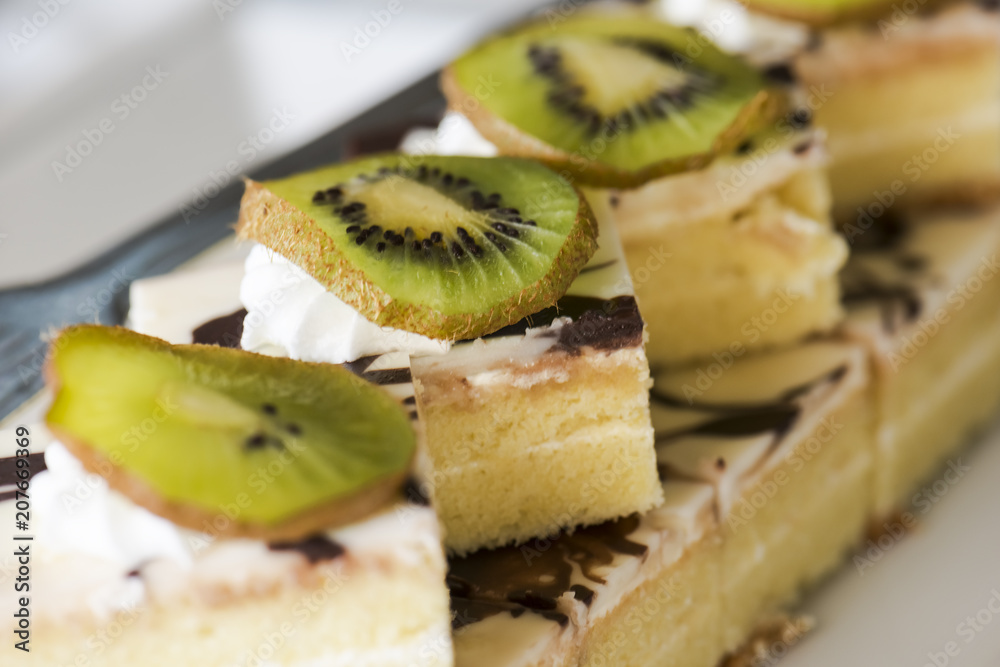 Сake decorated with cream and a slice of kiwi on a white plate. Selective focus Сake decorated with cream and a slice of kiwi on a white plate. Selective focus