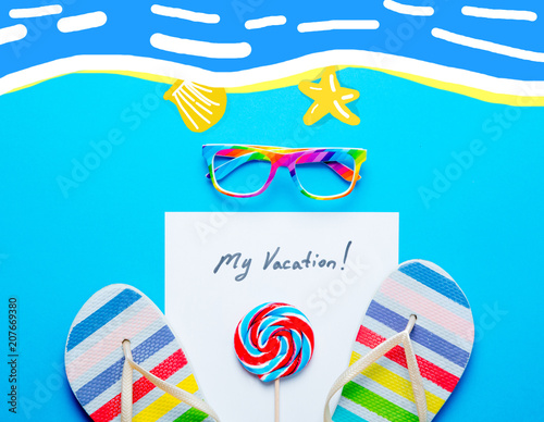 photo of sheet of paper My Vacation, lollipop, colorful sandals and glasses on the wonderful blue studio background photo