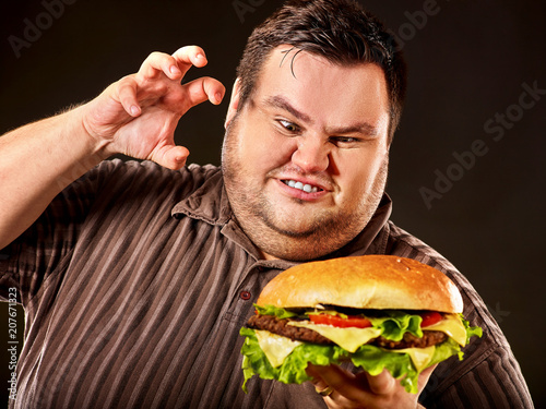 Diet failure of fat man eat fast food. Breakfast for mad overweight person who eating huge hamburger. Junk meal leads to obesity concept on black background. Feast for occasion.