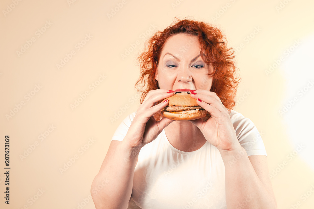 Big woman eat fast food. Red hair fat girl with burger. Unhealthy food concept with plus size female Big woman eat fast food. Red hair fat girl with burger. Unhealthy food concept with plus size female