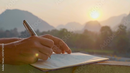 Young woman writing morning pages in diary outdoor, close-up photo