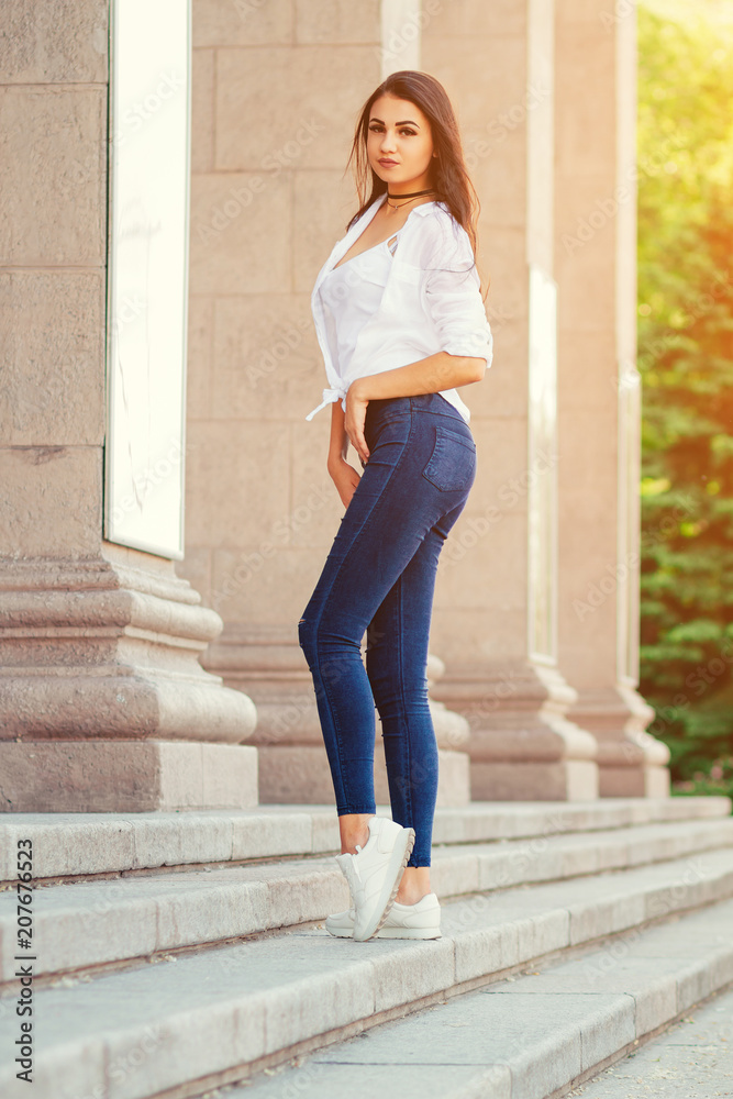 young stylish brunette girl posing in white shirt and jeans