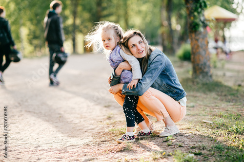 Happy smiling mother hugging her lovely little daughter outdoor. Lifestyle family. Adult cheerful female parent playing with her beautiful emotional child at nature in summer. Positive people faces.