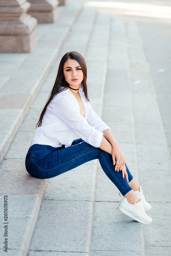 beautiful girl with long hair, fashionable girl in summer clothes, modern  lifestyle, sitting on the steps on the street Stock Photo