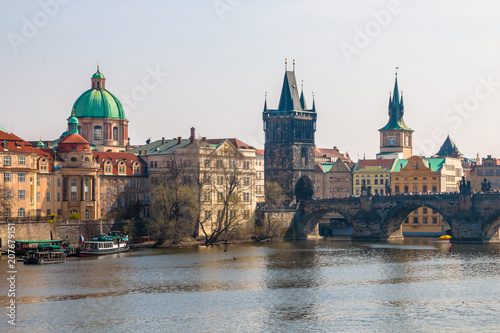 Charles Bridge, Old Town Bridge Tower and St Francis Of Assisi Church in a scenic view from Vltava river with cruise boats in Prague, Czech Republic