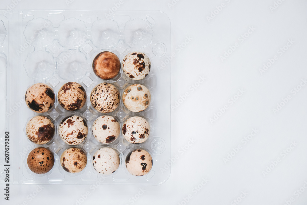 Uncooked scattered quail eggs in transparent box on white background Uncooked scattered quail eggs in transparent box on white background