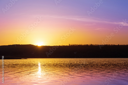 Dramatic sunset over river with orange and purple colors.Sun goes down over pond and forest silhouette. Beautiful nature background
