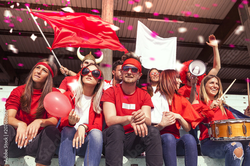 group of fans dressed in red color watching a sports event photo