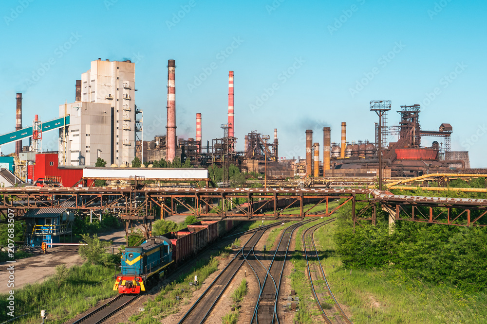 Cargo freight train wagons go on railroad in industrial zone with plants and manufacturing factories of heavy industry