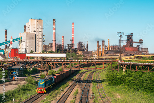 Cargo freight train wagons go on railroad in industrial zone with plants and manufacturing factories of heavy industry