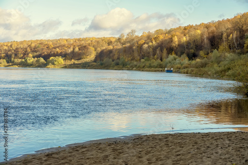 Lake, river on background of forest with yellow leaves, pier on water, sunny autumn day on the countryside, fall