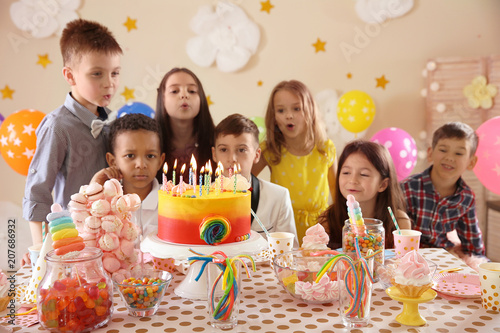 Cute children blowing out candles on birthday cake at table indoors