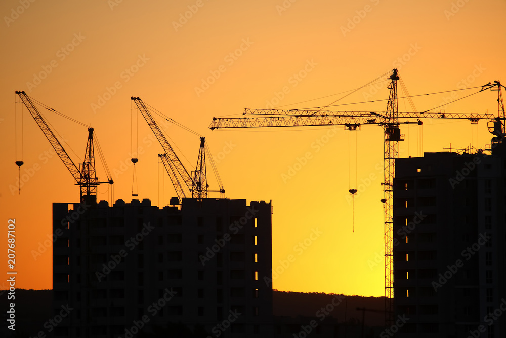 Construction cranes with built houses on the background of the sunset sky