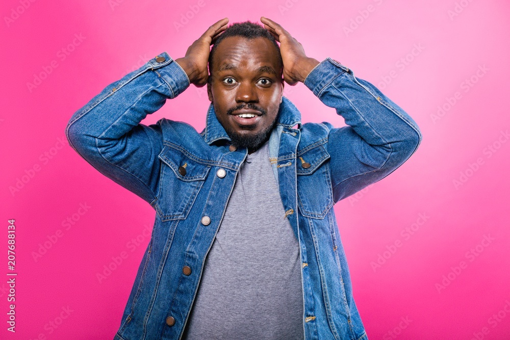 Emotional African man holding hands over head on pink background Emotional African man holding hands over head on pink background