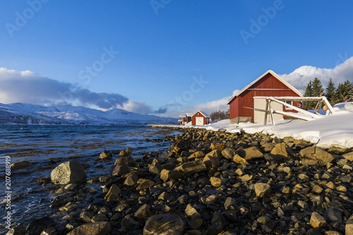 Typical norwegian warm and cosy house located at the lakeside at a fjord in a snowy winter landscape.