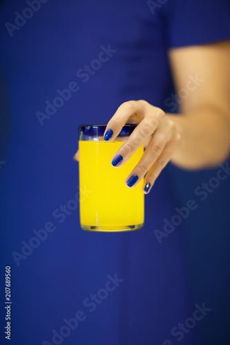 Beautiful woman hands holding glass of bright yellow orange soda in front of her blue dress, can be used as background