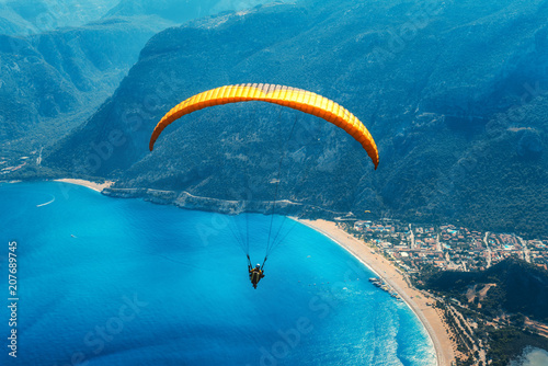 Fototapeta Naklejka Na Ścianę i Meble -  Paragliding in the sky. Paraglider tandem flying over the sea with blue water, beach and mountains in sunrise. Aerial view of paraglider and Blue Lagoon in Oludeniz, Turkey. Extreme sport. Landscape