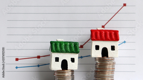 Housing price rising and differentiated concept. A miniature house on a pile of coins in front of a graph. photo