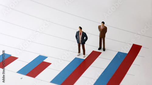 Miniature people standing on a bar graph. Numerical value and people's relationship concepts.