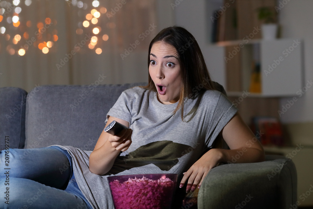 Obraz premium Amazed woman watching tv in the night at home