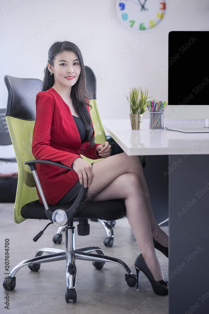 businesswoman in red suit smiling and sitting in office, looking at camera businesswoman in red suit smiling and sitting in office, looking at camera